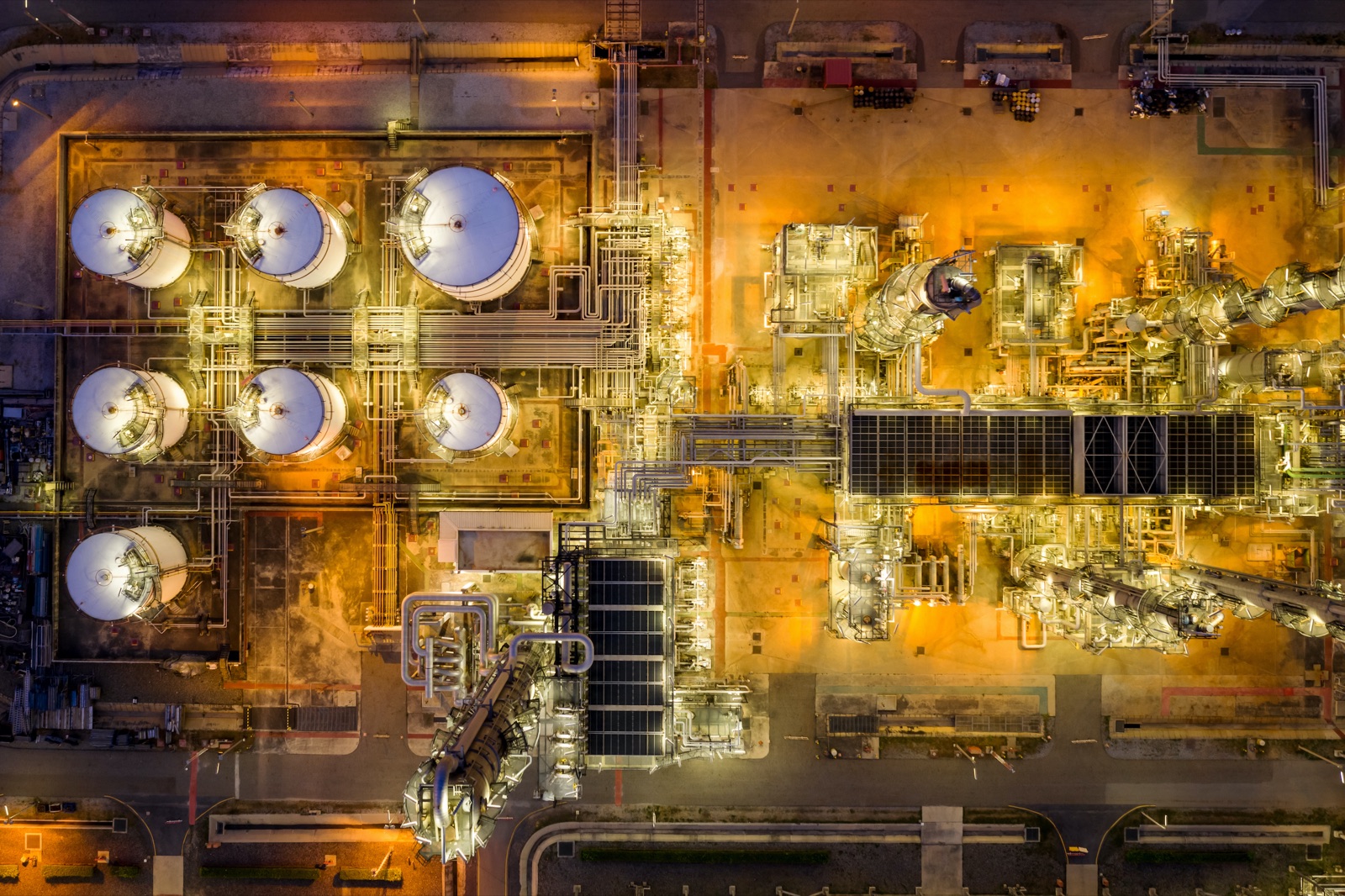 Aerial view of an industrial processing plant at night with storage tanks and illuminated process units.